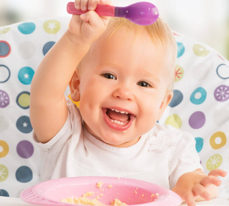 smiling baby holding a spoon over her head