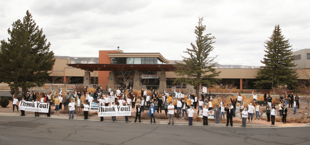 Group of hospital employees holding "thank you" signs in front of the hospital